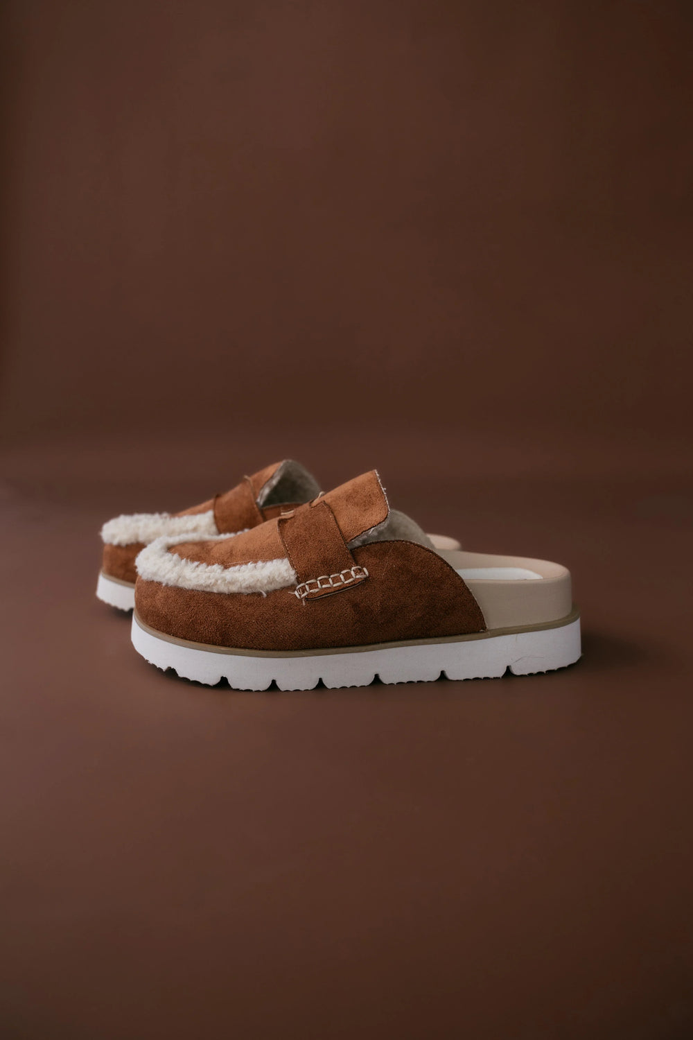Pair of brown suede shoes with white soles on a brown background