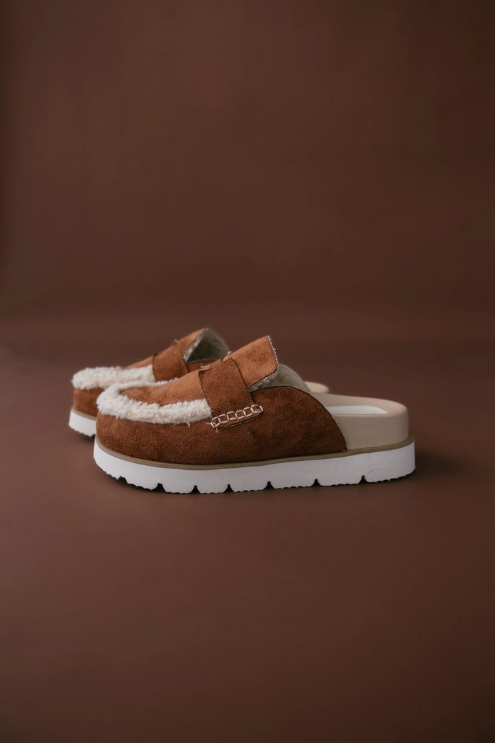 Pair of brown suede shoes with white soles on a brown background