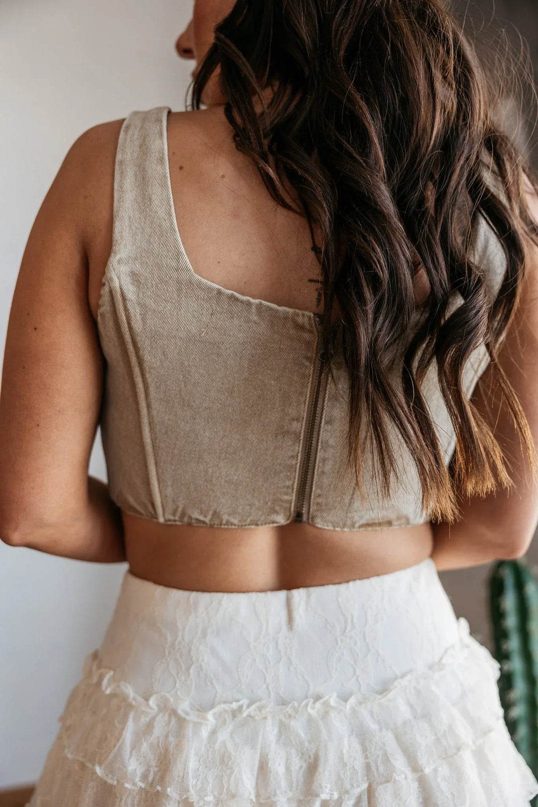 Woman wearing a beige sleeveless top and white skirt with braided hair.