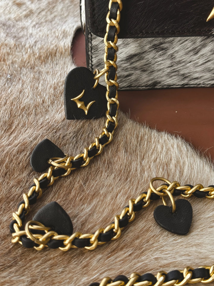 Gold chain with black heart-shaped pendants on a textured surface