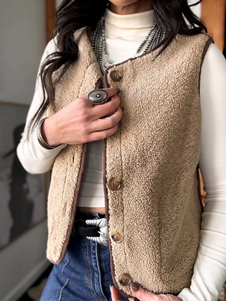 Person wearing a beige fleece vest over a white shirt with a blurred background