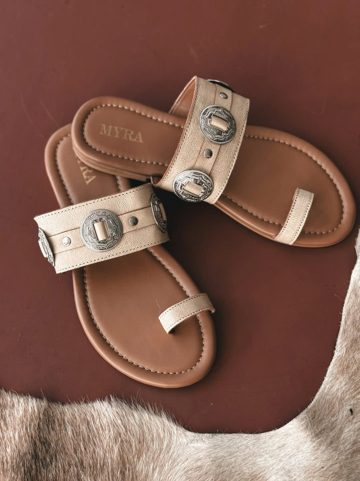 Pair of tan sandals with decorative straps on a brown surface
