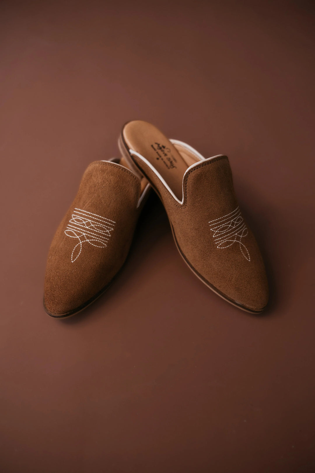 Pair of brown suede slippers with white embroidery on a brown background