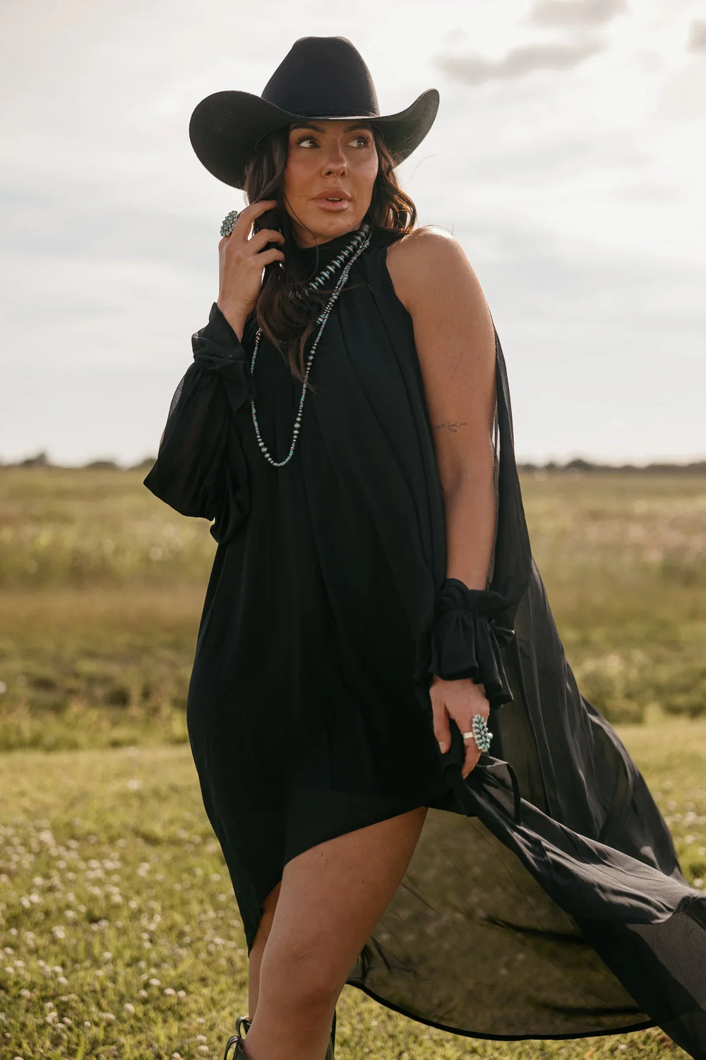 Woman in a black dress and hat standing in a field