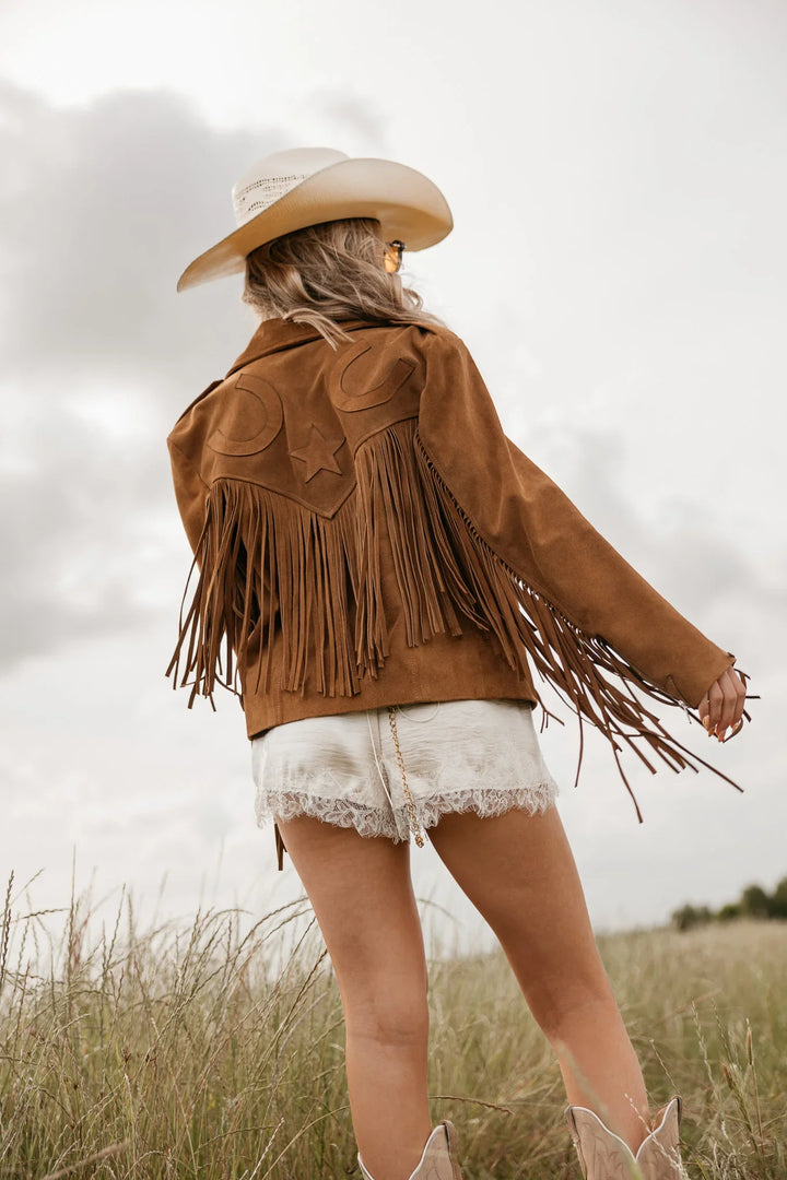 Person wearing a brown fringed jacket and cowboy hat in a field