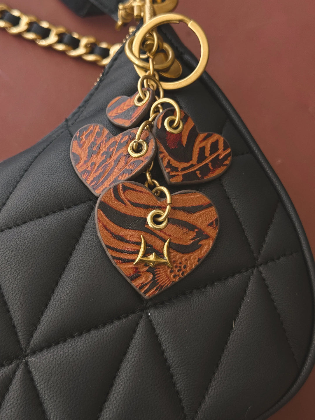 Black quilted handbag with heart-shaped leather charms on a brown background