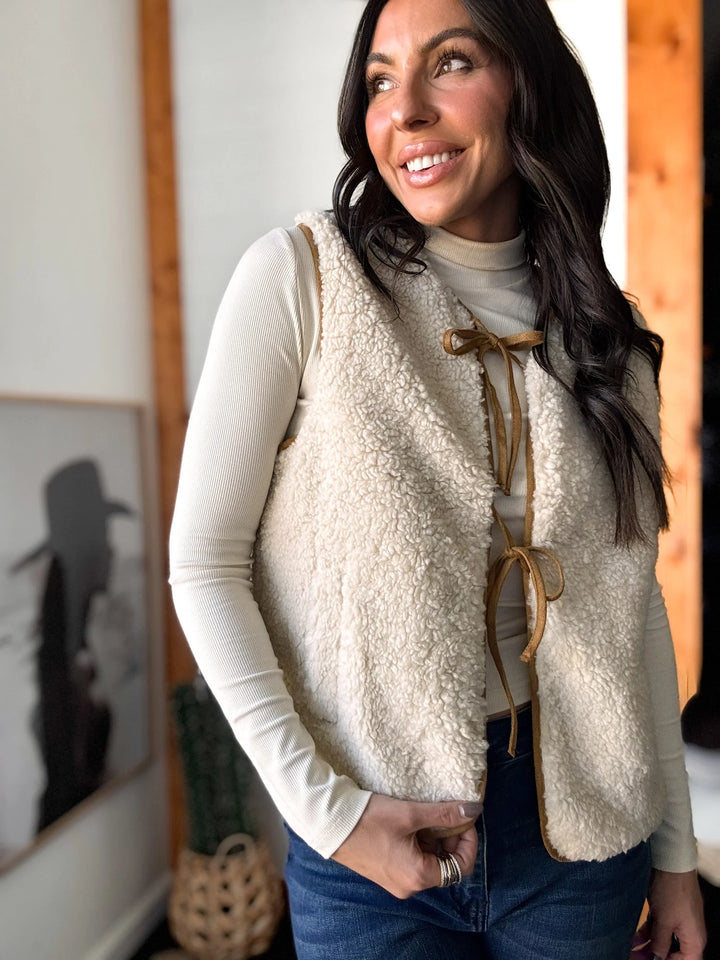 Woman wearing a cream-colored fleece vest with a wooden latch in a room setting.