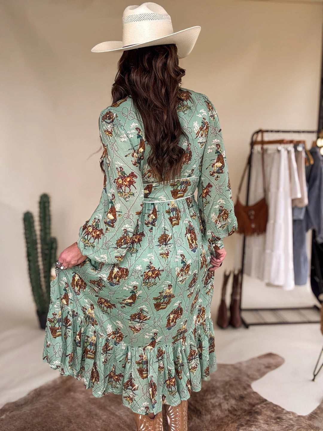 Woman in a cowgirl hat and sage green western print dress with ruffle hem, western boots
