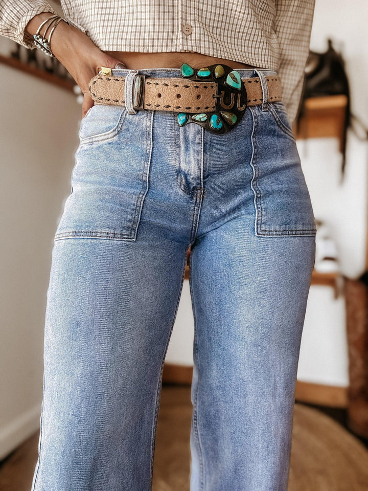 Woman wearing high-waisted flare jeans, a boho turquoise belt, and a plaid blouse.