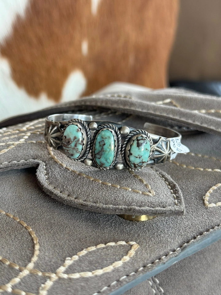 Western turquoise silver cuff bracelet with three stones on suede cowboy boot, cowhide background