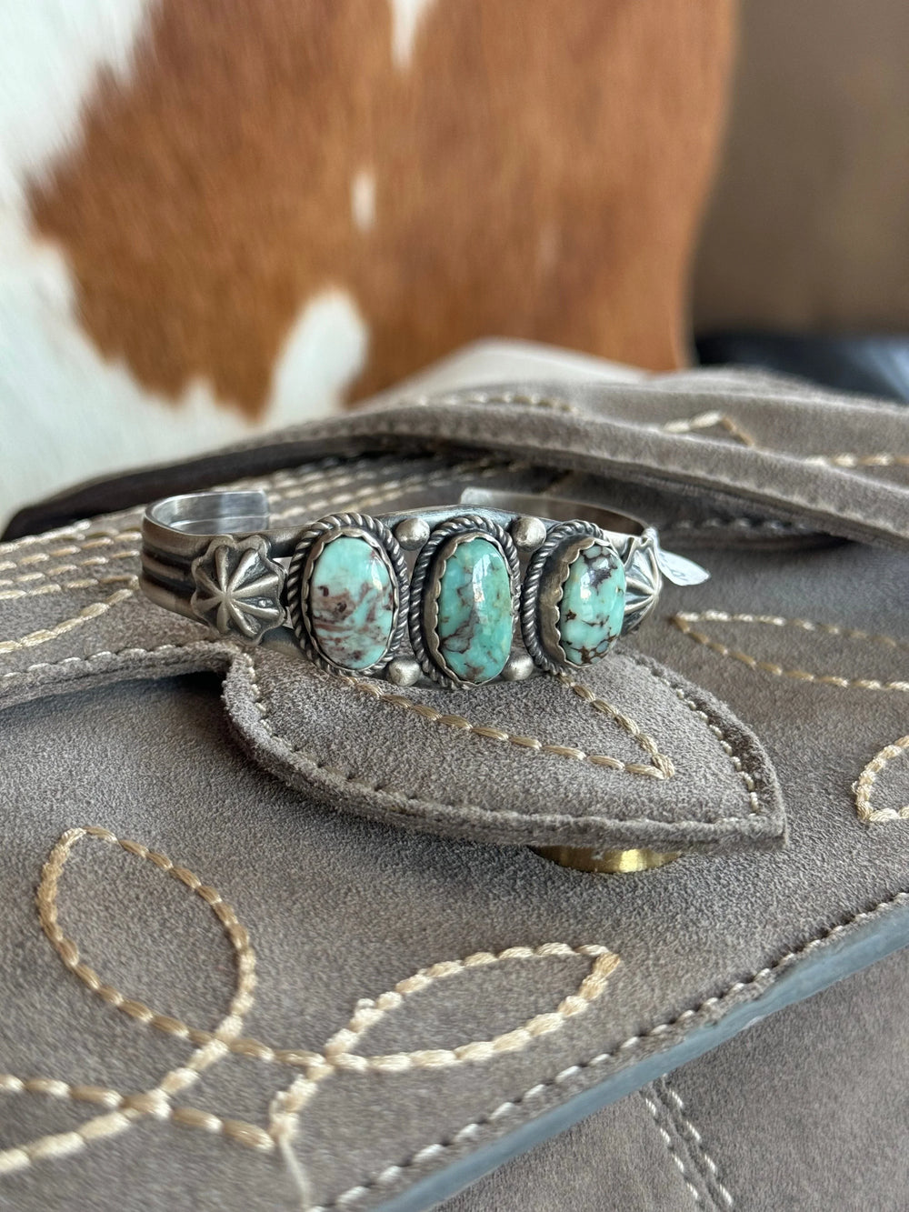 Turquoise western boho cuff bracelet on embroidered suede clutch with cowhide background