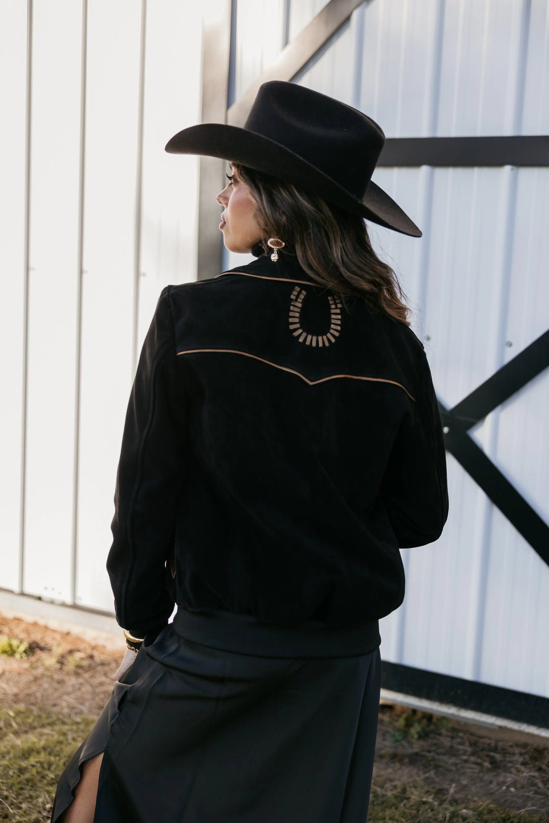 Woman in black western hat and jacket with horseshoe detail, boho cowgirl style outdoors