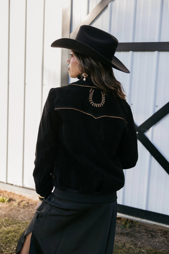 Woman in black western hat and jacket with horseshoe detail, boho cowgirl style outdoors