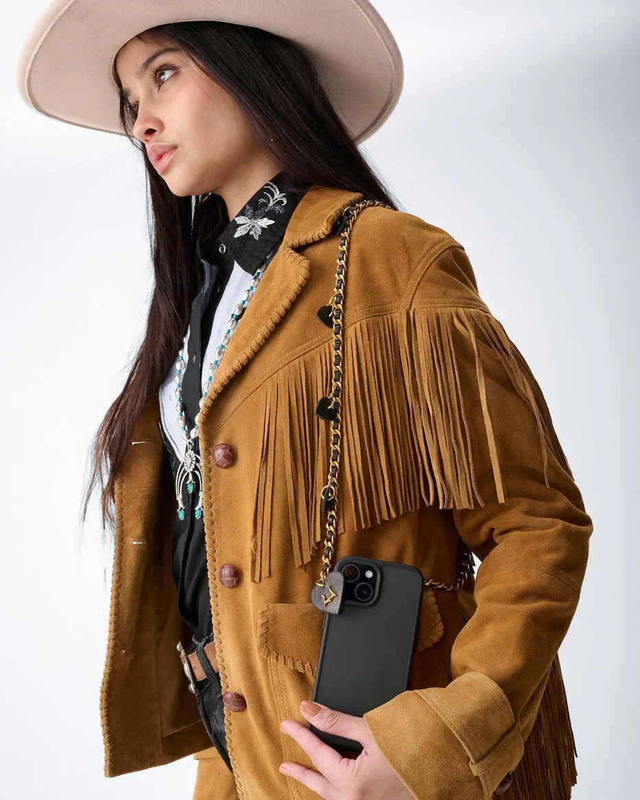 Woman wearing a brown fringed jacket and beige hat, holding a phone with a white background