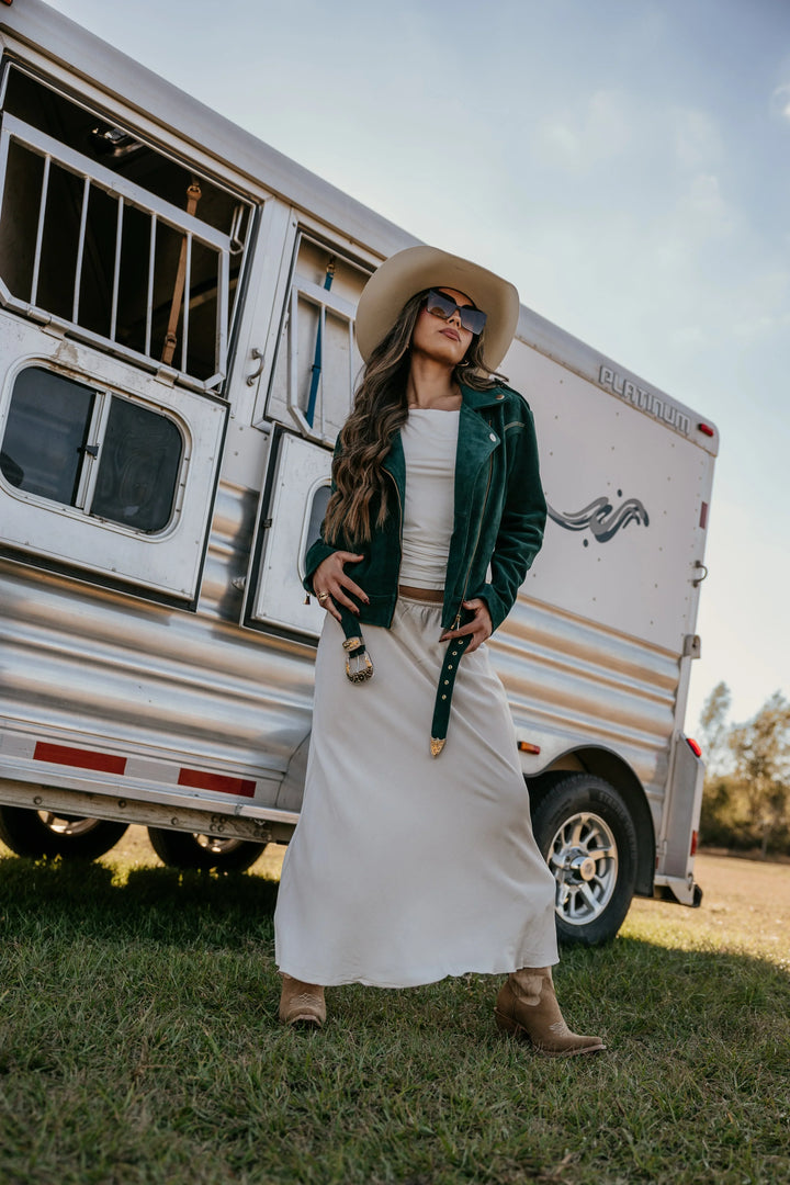 Woman in western boho outfit with suede jacket, maxi skirt, cowboy hat and boots by horse trailer