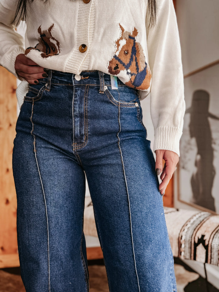 Woman wearing high-waisted wide leg jeans and a white sweater with horse design, western style