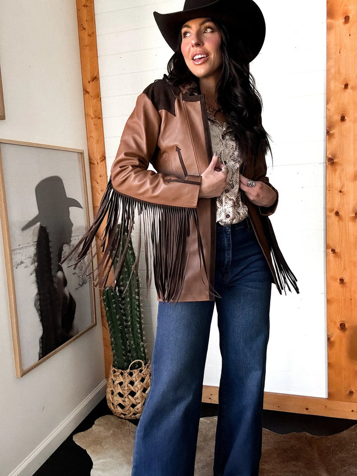 Woman in western fringe leather jacket, wide leg jeans, and black cowboy hat indoors
