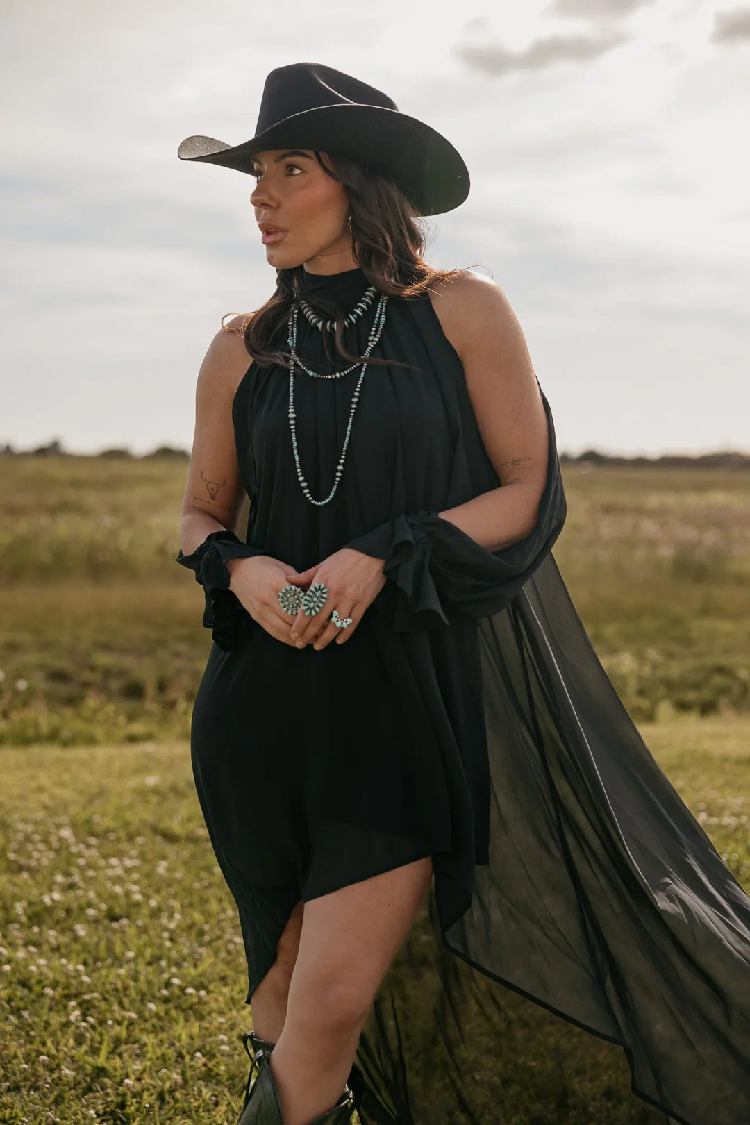Woman in a black dress and hat standing in a field