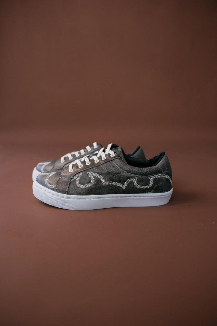 Western-inspired brown sneakers with decorative stitching and white soles on brown background