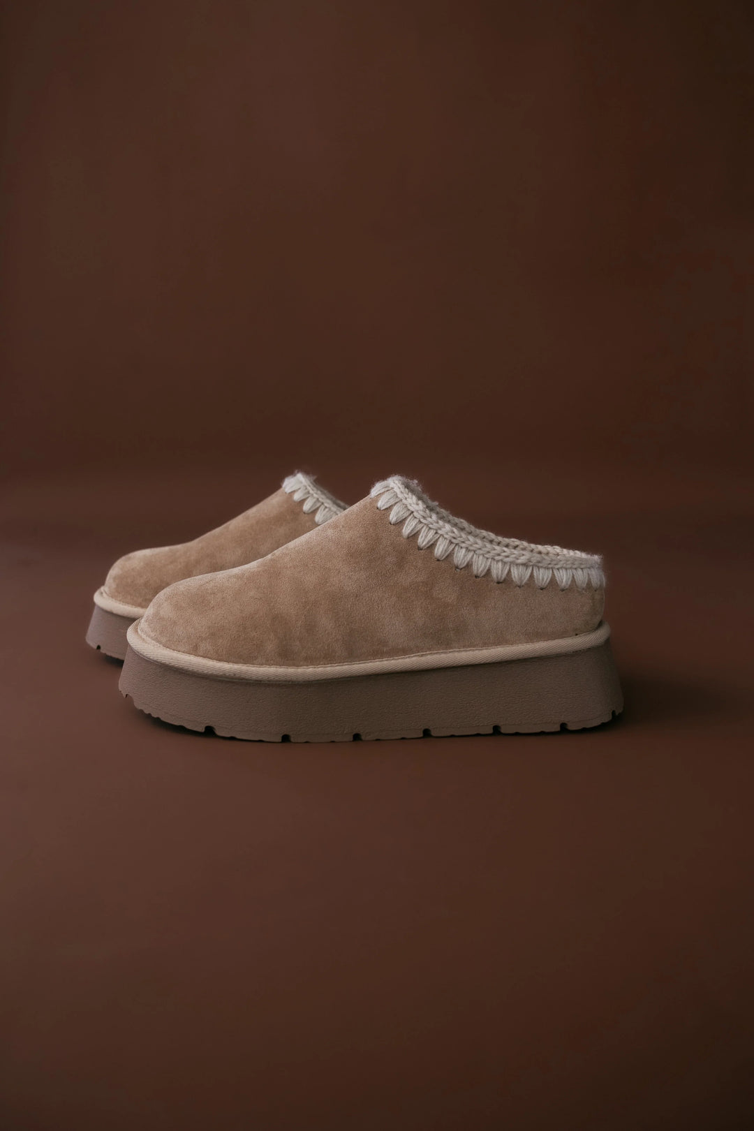 Pair of beige slippers with white trim on a brown background