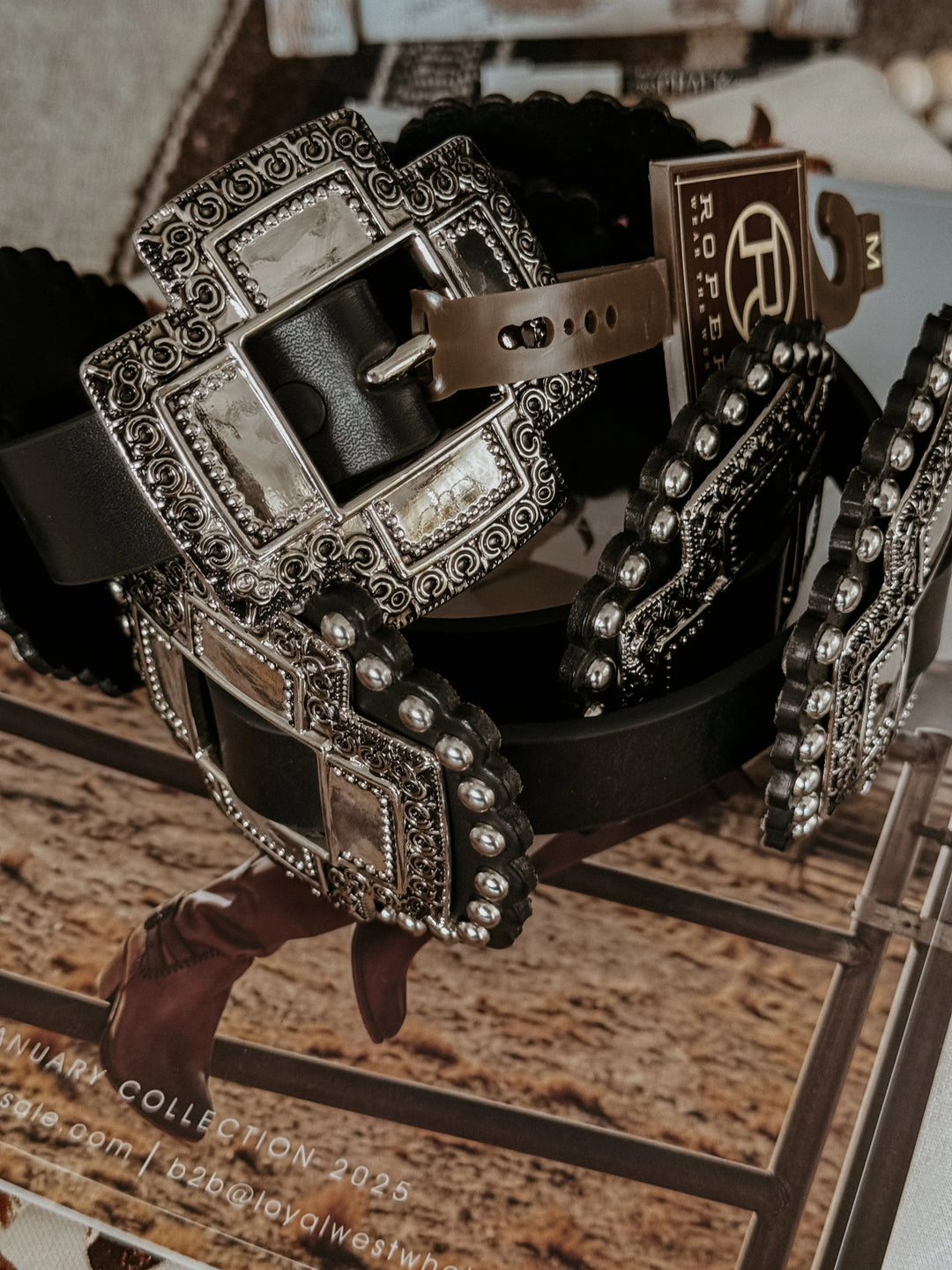 Black western belt with large ornate silver buckle and studs, styled on rustic background.