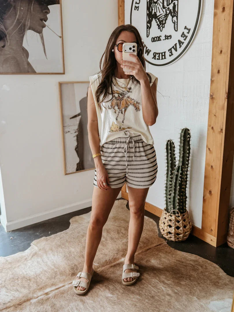Woman taking a mirror selfie in a room with framed artwork and a cactus plant.