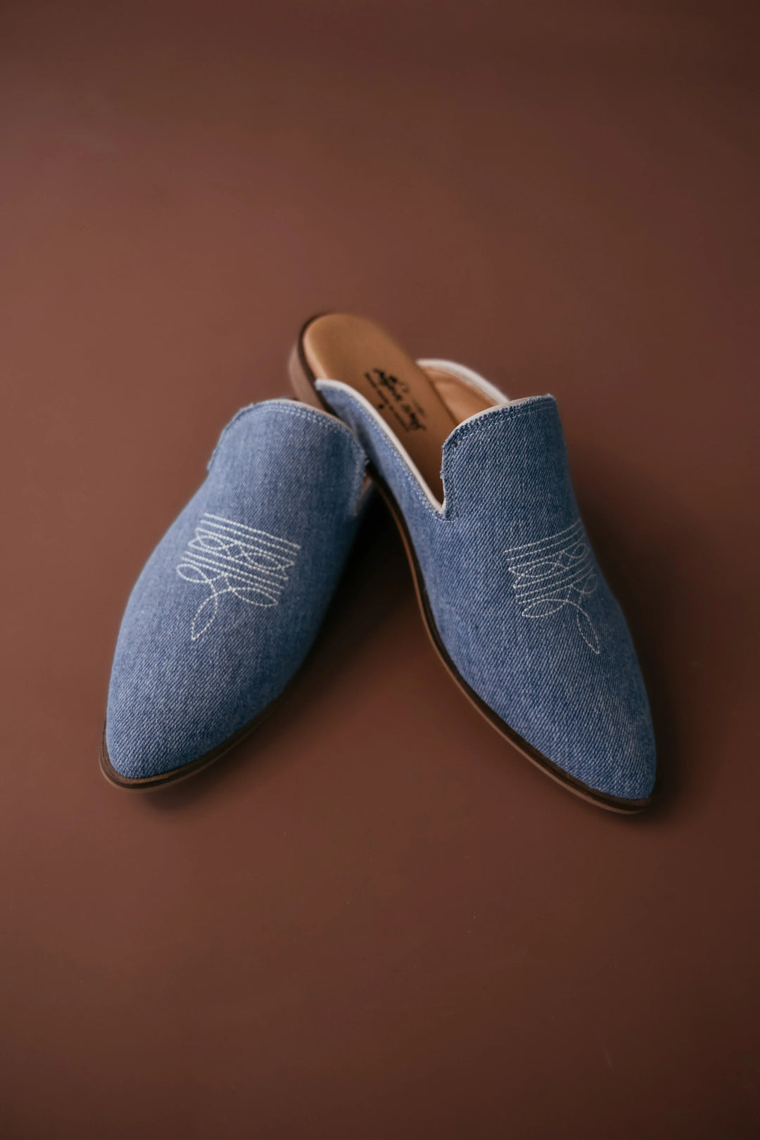 Pair of blue loafers with white embroidery on a brown background