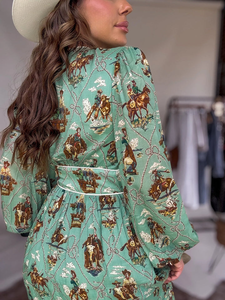 Woman wearing a green western boho dress with cowboy and rodeo print, white hat