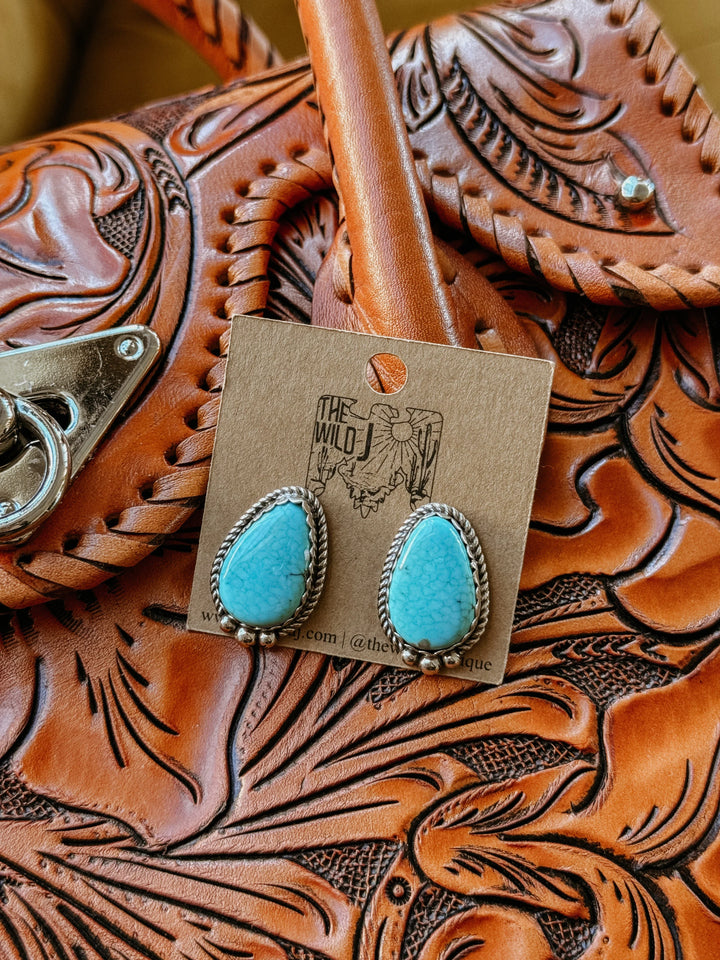 Turquoise western earrings with silver rope detail on tooled leather purse background