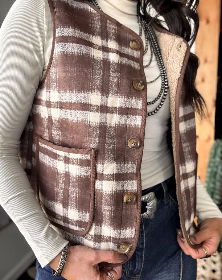 Person wearing a brown plaid vest over a white shirt with a blurred background