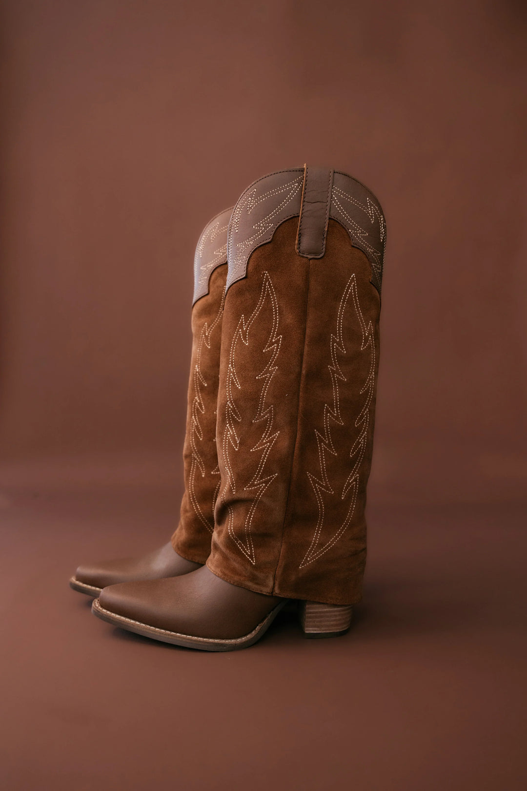 Pair of brown cowboy boots with white stitching on a brown background