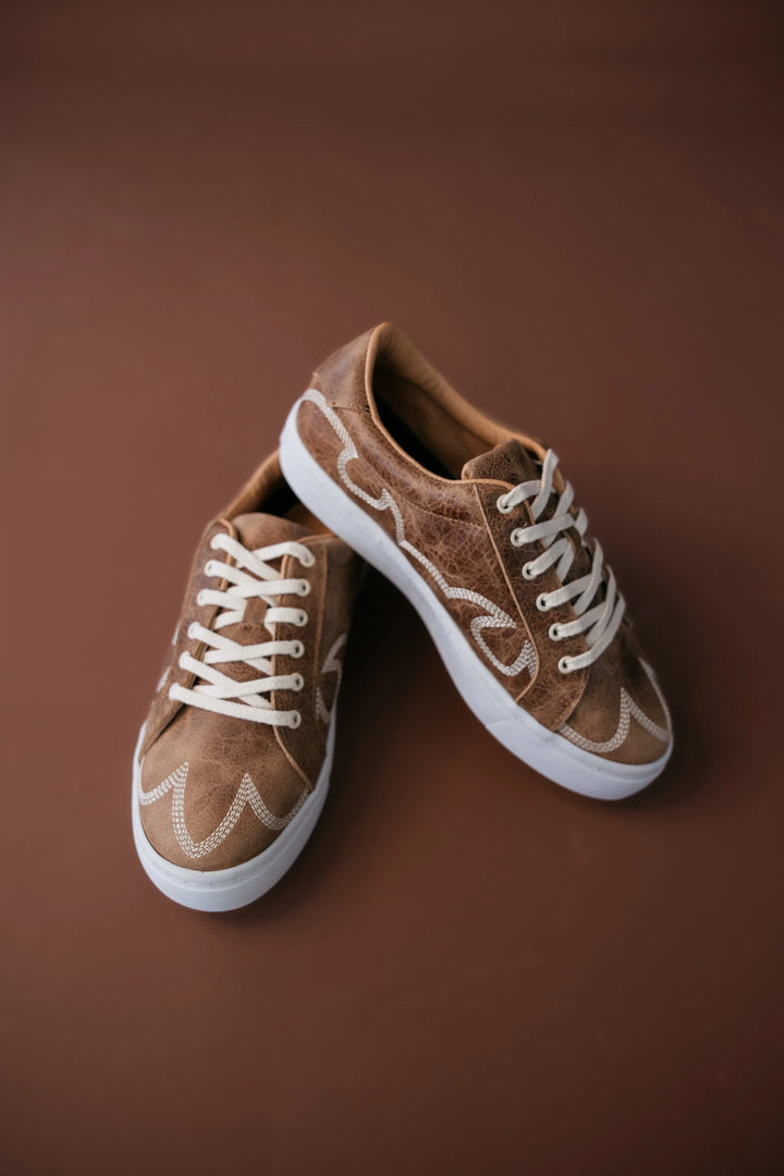 Pair of brown sneakers with white laces on a brown background