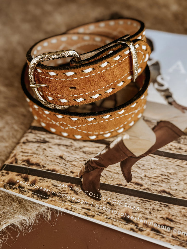 Brown suede western belt with tooled silver buckle and white stitching on rustic background.