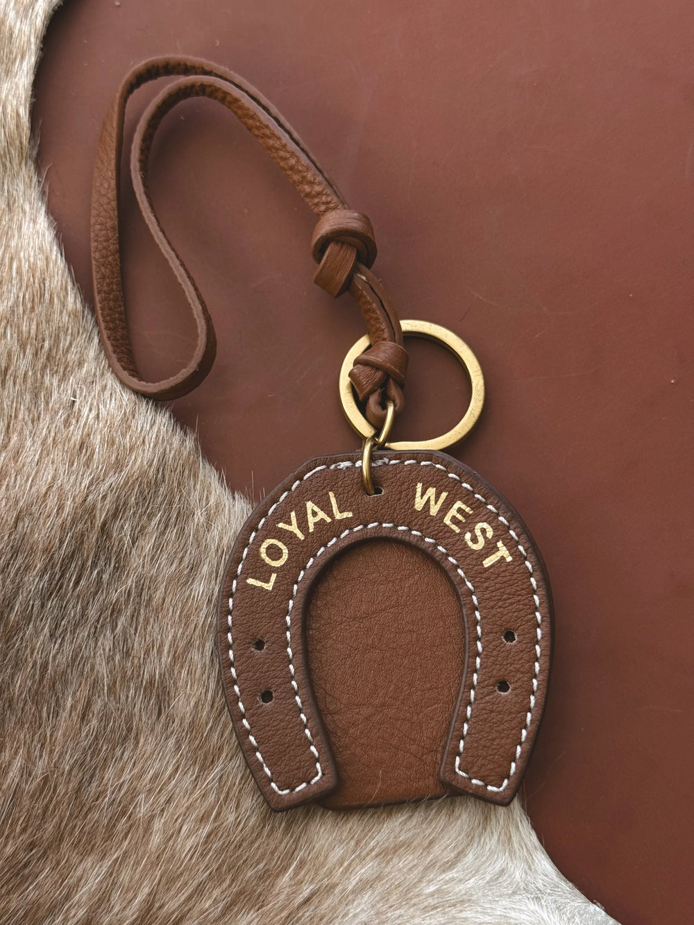 Brown leather keychain with 'LOYAL WEST' text on a fur background