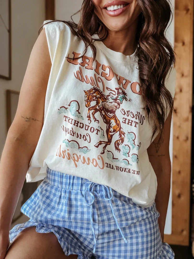 Woman wearing a sleeveless graphic top with a horse design and checkered shorts indoors.