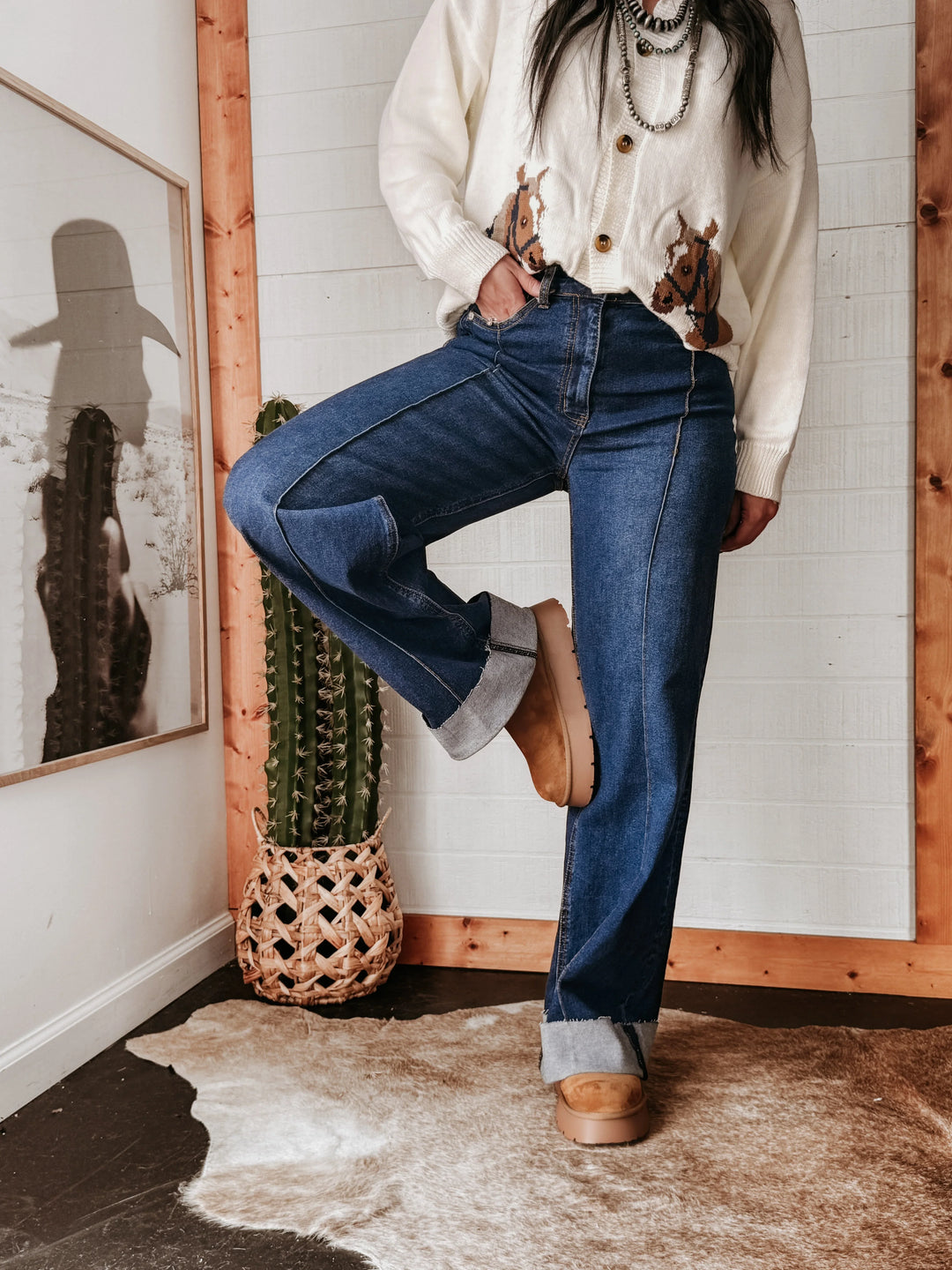 Woman modeling high rise hem jeans with rolled cuffs, western boots and cowgirl sweater