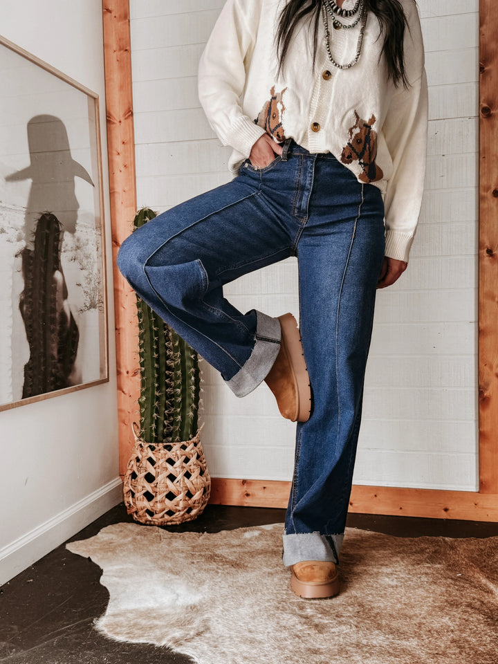 Woman modeling high rise hem jeans with rolled cuffs, western boots and cowgirl sweater