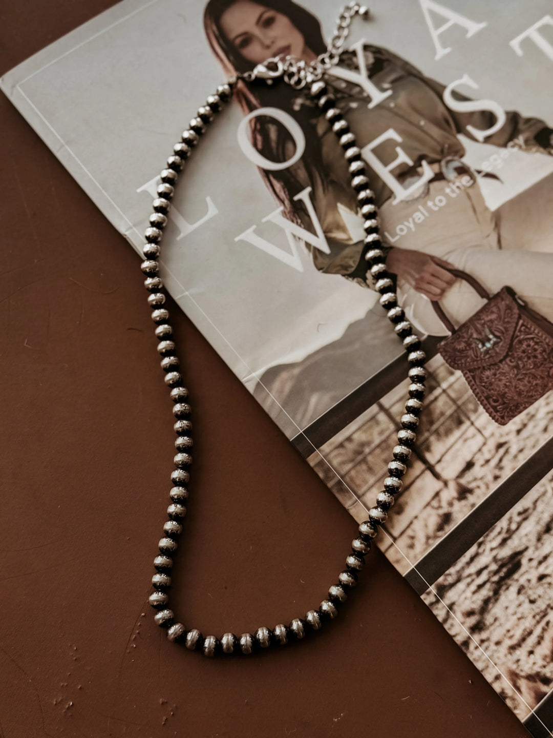Silver beaded western necklace on a fashion magazine and brown surface background