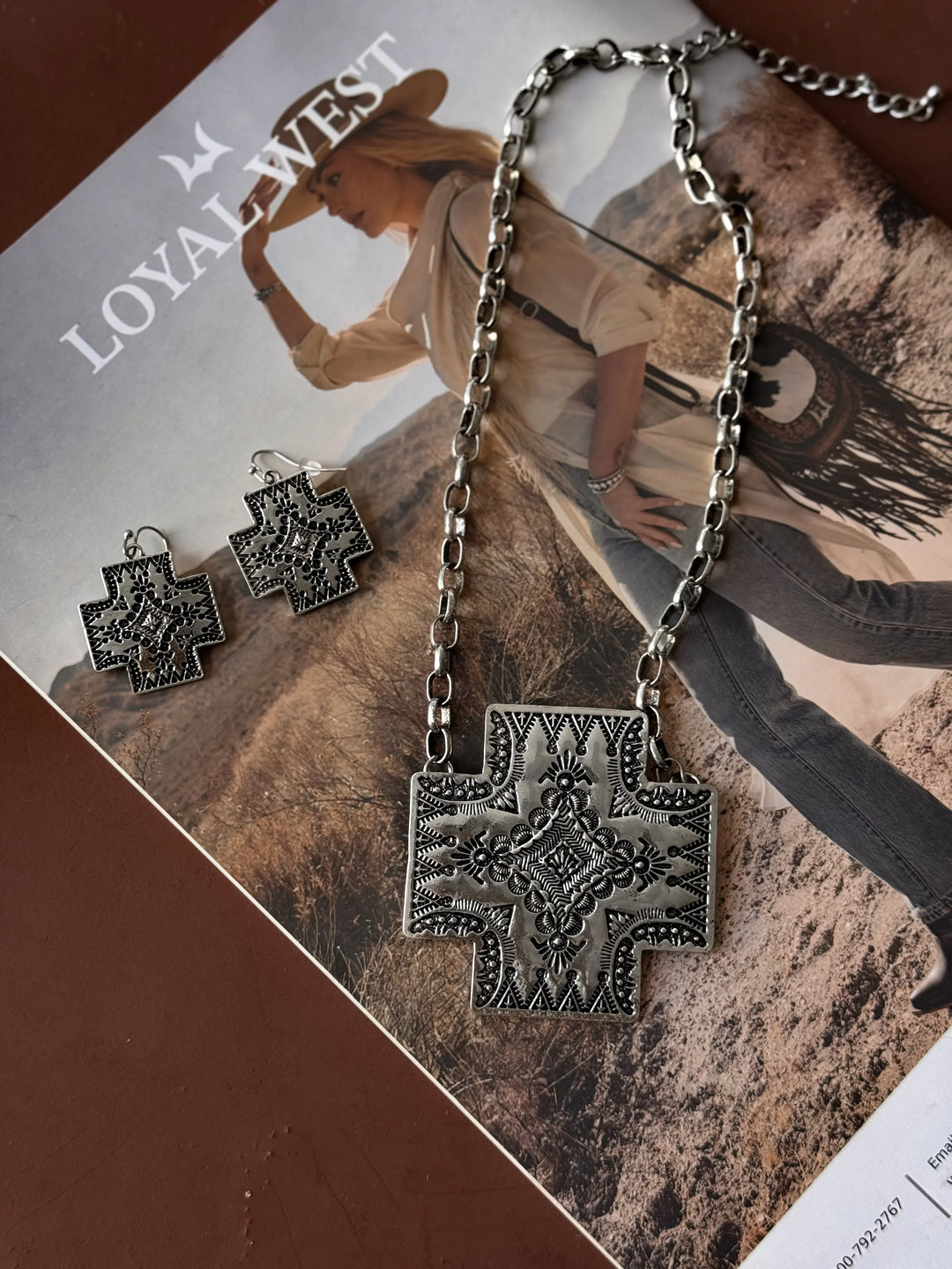 Silver cross necklace and earrings on a magazine with a cowboy graphic.