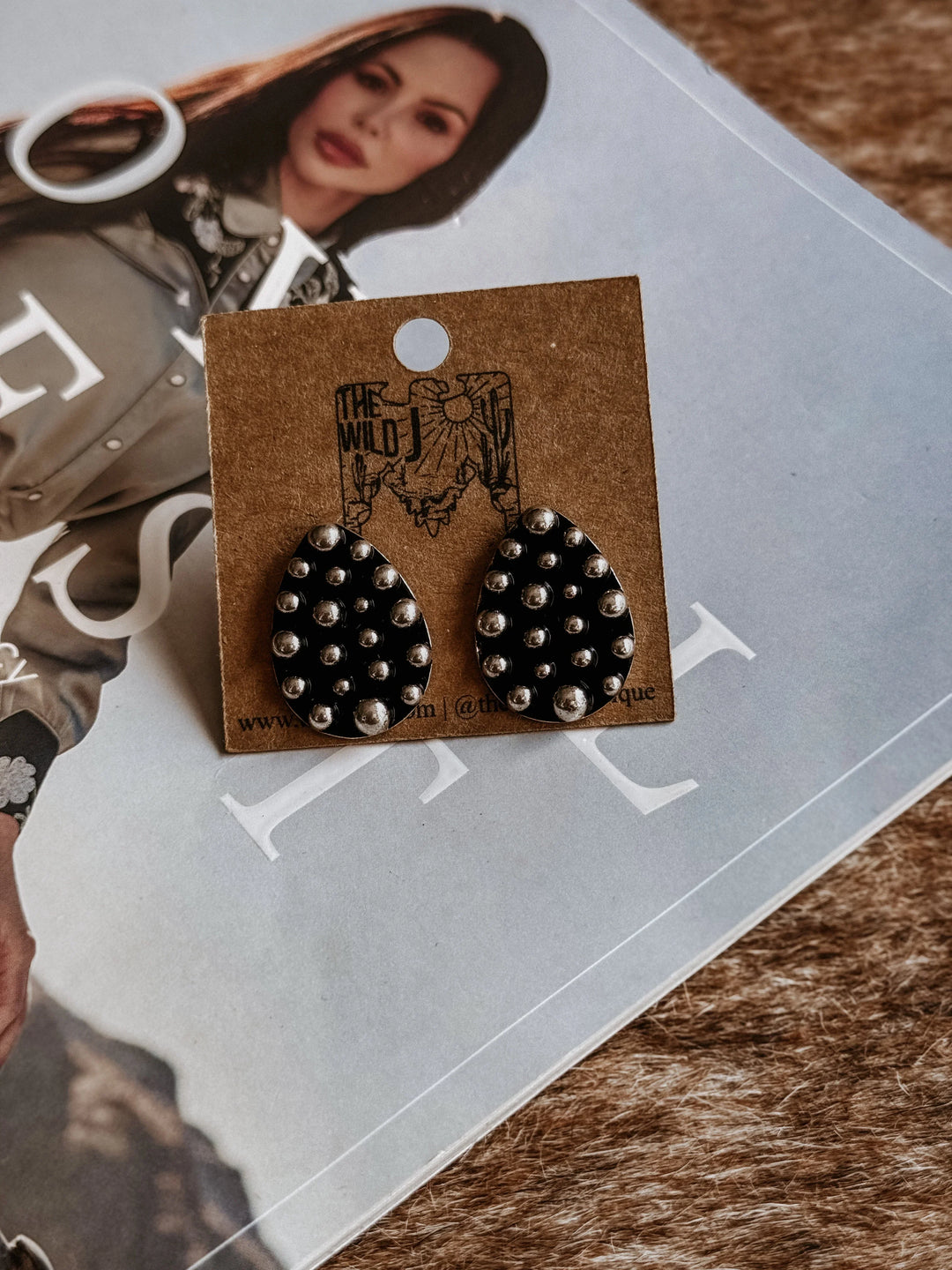 Black studded earrings on a branded card with a magazine in the background