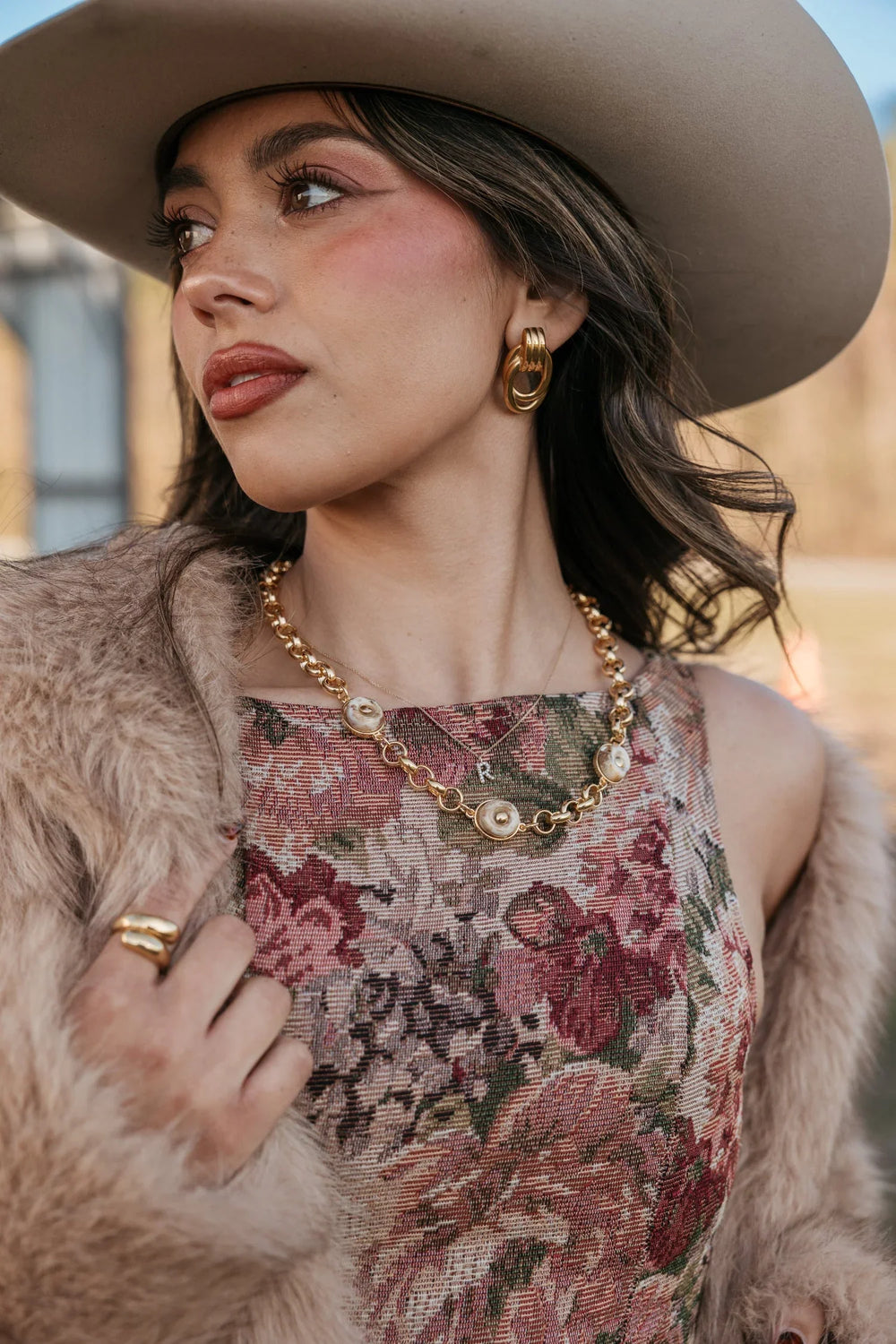 Woman wearing a floral dress, fur coat, and wide-brimmed hat outdoors.